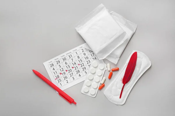 Menstruationskalender mit femininen Produkten und Pillen auf grauem Hintergrund — Stockfoto