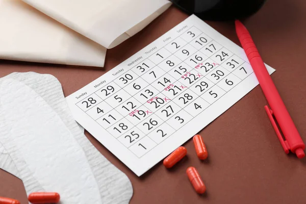 Calendario menstrual con productos femeninos y pastillas sobre fondo de color — Foto de Stock