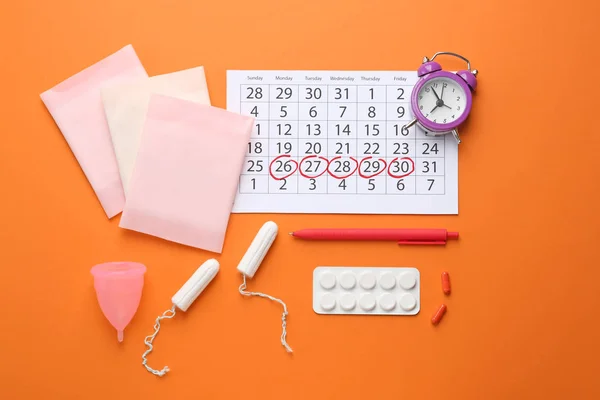 Менструальный календарь с женскими продуктами, таблетками и будильником на цветном фоне — стоковое фото