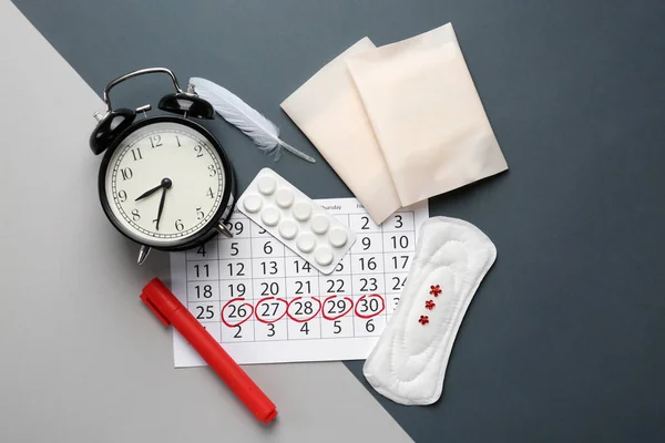 Menstrual calendar with feminine products, pills and alarm clock on grey background — Stock Photo, Image