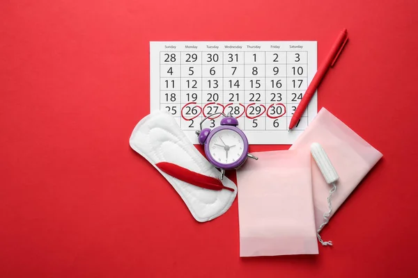 Менструальный календарь с женскими продуктами и будильником на цветном фоне — стоковое фото