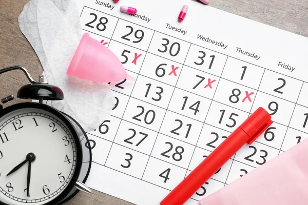 Calendario menstrual con productos femeninos, pastillas y despertador sobre fondo gris — Foto de Stock