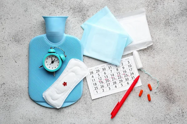 Менструальний календар з жіночими продуктами, таблетками, водяним мішком і будильником на сірому фоні — стокове фото