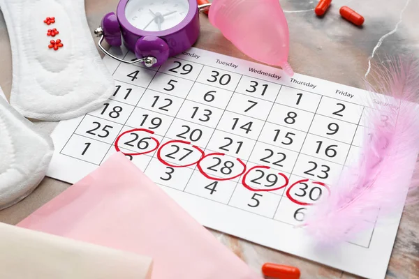 Менструальный календарь с женскими продуктами, таблетками и будильником на сером фоне — стоковое фото
