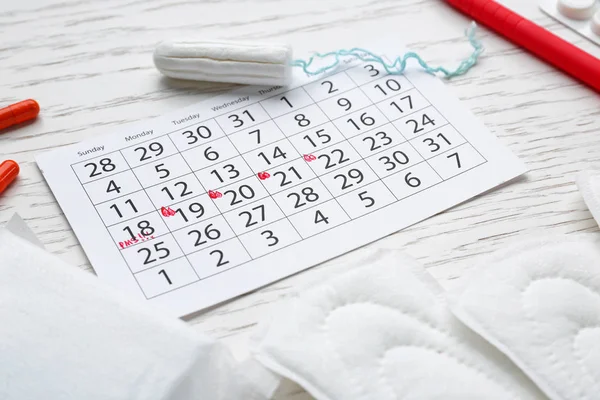 Menstrual calendar with feminine products and pills on white table — Stock Photo, Image