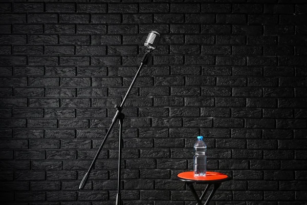 Microfoon met kruk en fles water op donkere baksteen achtergrond — Stockfoto
