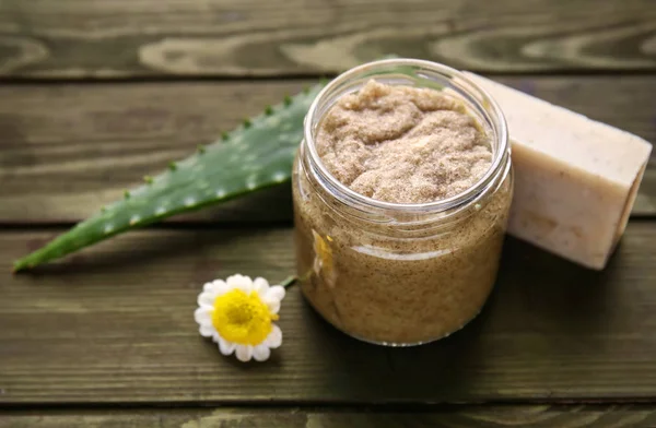 Jar with sugar scrub and soap on wooden table