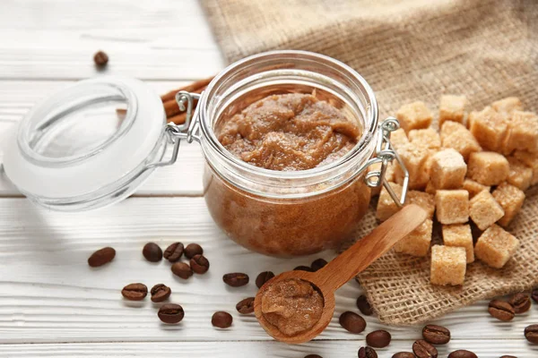 Jar with sugar scrub and ingredients on white table