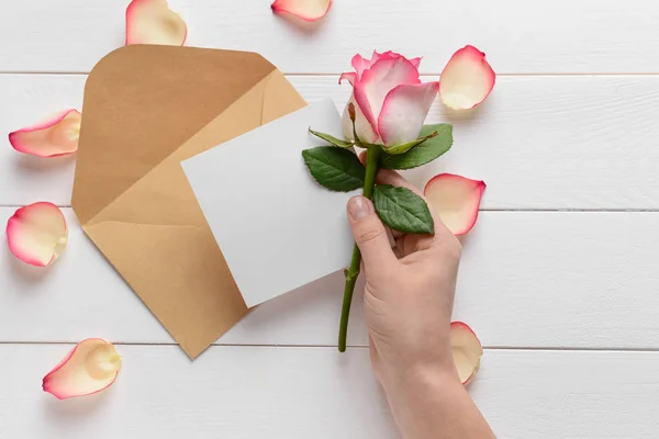 Main féminine avec invitation et fleur sur fond de bois blanc — Photo