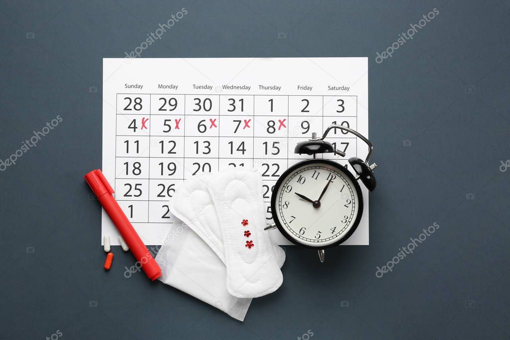 Menstrual calendar with pads and alarm clock on dark background