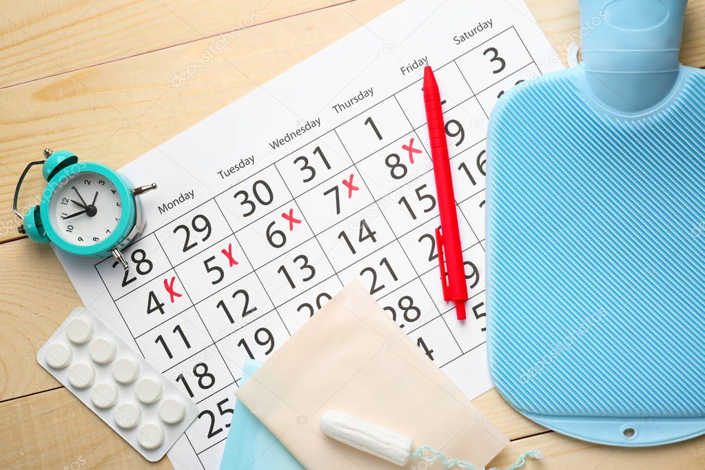 Menstrual calendar with feminine products, pills, water bag and alarm clock on wooden background