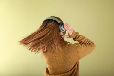 Kulaklıklı genç bir kadın arka planda müzik dinliyor.