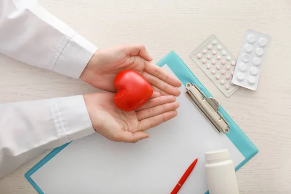 Cardiologist with red heart at table in clinic — Stock Photo, Image