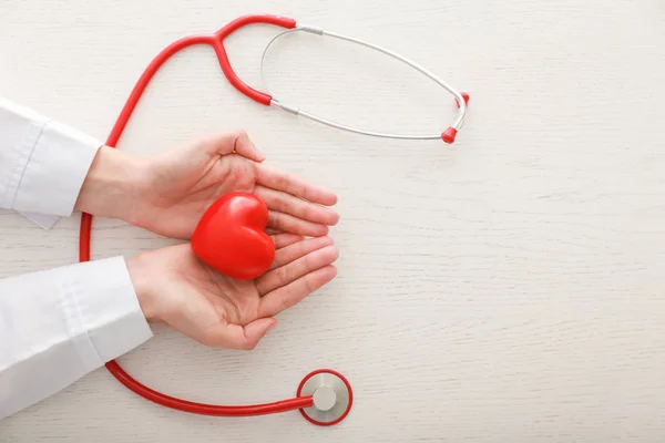 Kardiolog z czerwonym sercem i stetoskopem przy stole — Zdjęcie stockowe
