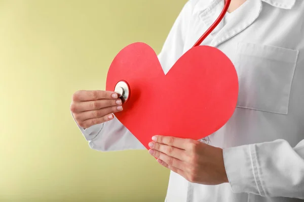Kardiologe mit rotem Herz und Stethoskop auf farbigem Hintergrund — Stockfoto