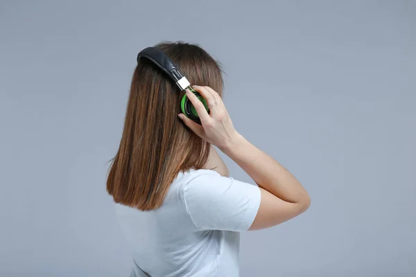 Young woman with headphones listening to music on grey background — Stock Photo, Image