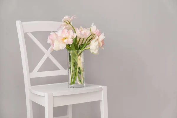 Bouquet of beautiful tulips on chair against grey background — Stock Photo, Image