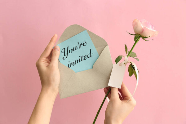 Руки женщины с приглашением и цветком на цветном фоне
