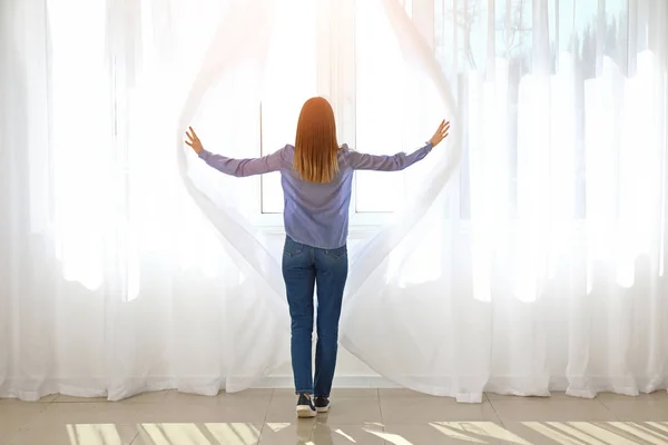 Jonge vrouw het openen van licht gordijnen thuis — Stockfoto