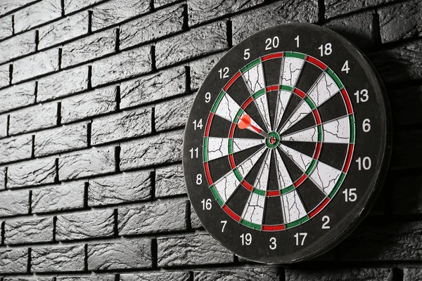 Dartboard with hit bullseye on dark brick wall — Stock Photo, Image