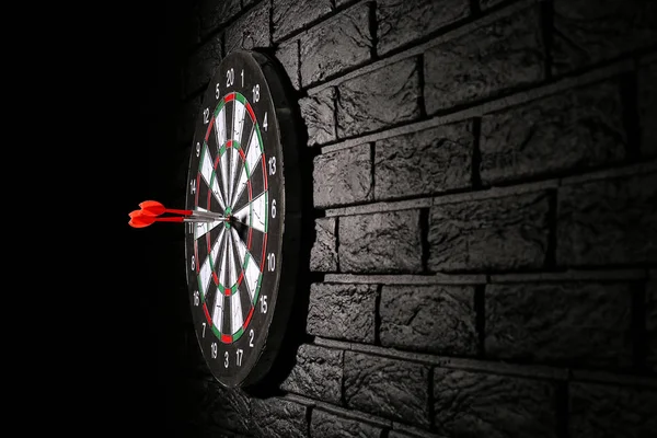 Dartboard com bullseye hit na parede de tijolo escuro — Fotografia de Stock