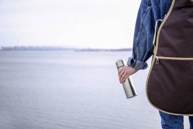 Nehir kenarında termos ve gitar olan kadın, arka görünüm