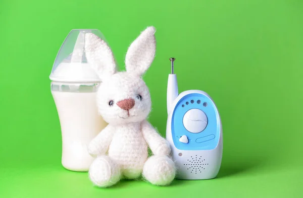 Modern baby monitor with toy and bottle of milk on color background — Stock Photo, Image