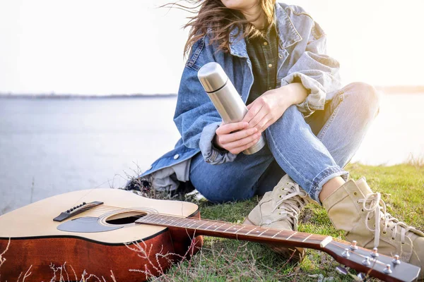 Vrouw met Thermos en gitaar zitten in de buurt van de rivier — Stockfoto