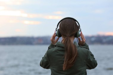 Genç kadın Nehri yakınında müzik dinlemek