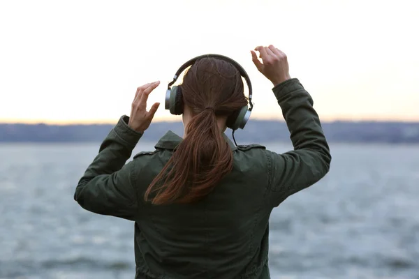 Jovem mulher ouvindo música perto do rio — Fotografia de Stock
