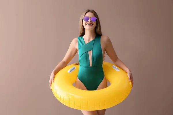 Schöne junge Frau in Badeanzug und mit aufblasbarem Ring auf farbigem Hintergrund — Stockfoto