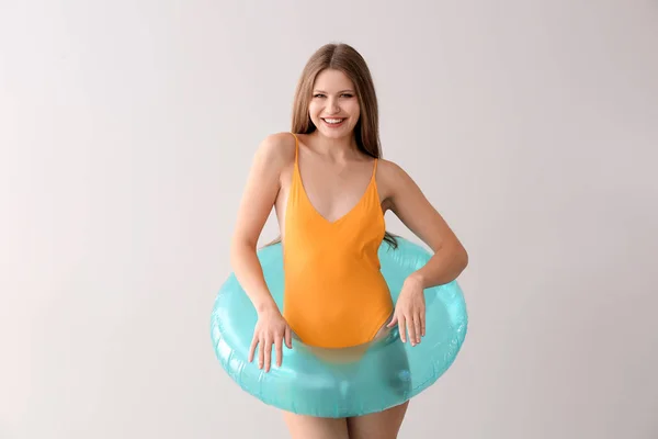 Mooie jonge vrouw in zwempak en met opblaasbare ring op lichte achtergrond — Stockfoto