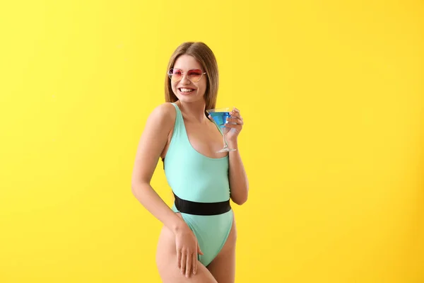 Schöne junge Frau in Badeanzug und mit Cocktail auf farbigem Hintergrund — Stockfoto