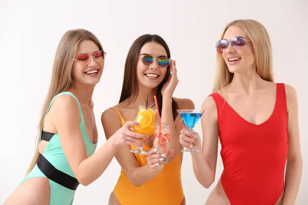 Beautiful young women in swimming suits and with cocktails on white background — Stock Photo, Image