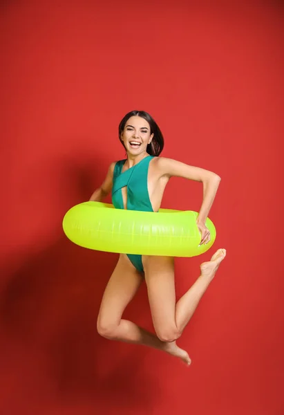 Springende junge Frau im Badeanzug und mit aufblasbarem Ring auf farbigem Hintergrund — Stockfoto