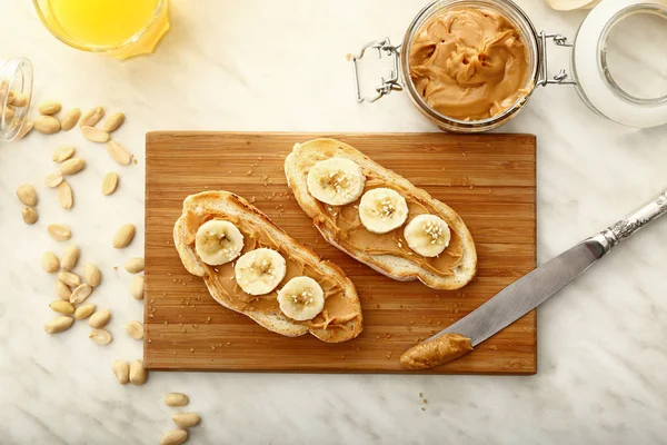 Bread with tasty peanut butter and banana on wooden board — Stock Photo, Image