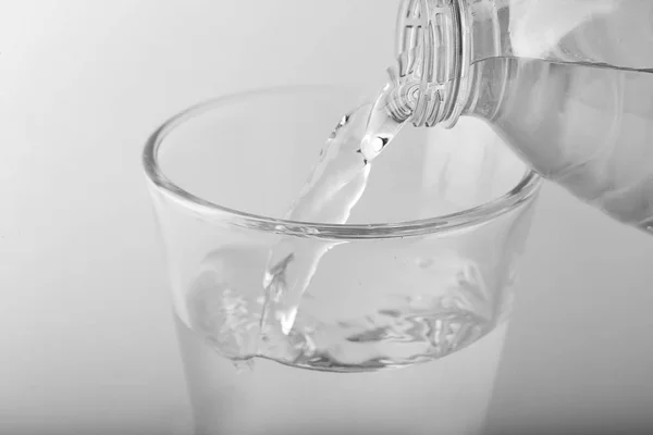 Pouring of water into glass on light background, closeup — Stock Photo, Image