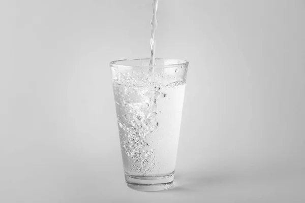 Verter agua en un vaso sobre un fondo claro — Foto de Stock