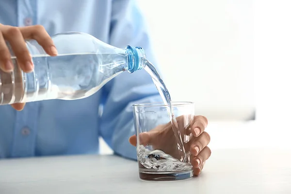 Mulher derramando água em vidro na mesa — Fotografia de Stock
