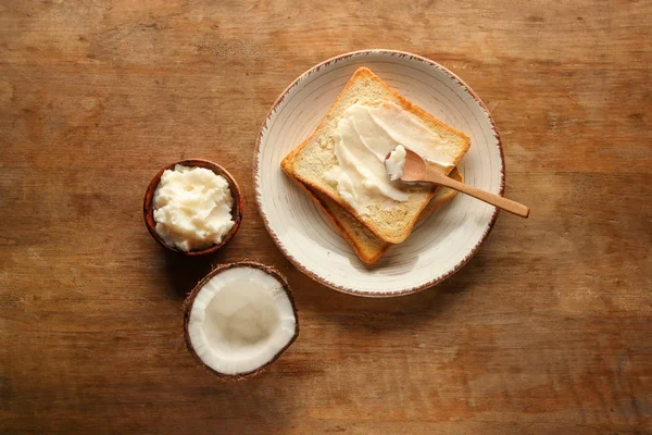 Coconut oil with tasty toasted bread on wooden table — Stock Photo, Image