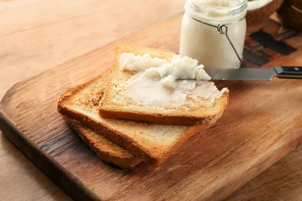 Coconut oil with tasty toasted bread on wooden board, closeup — Stock Photo, Image