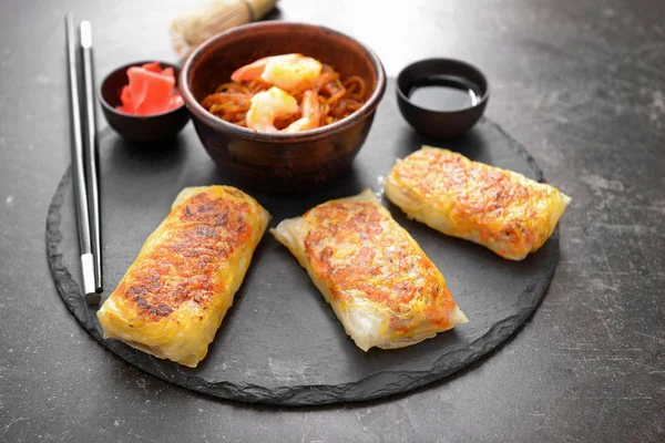 Slate plate with tasty fried spring rolls on table