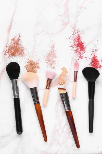 Different makeup brushes with cosmetics on light background — Stock Photo, Image