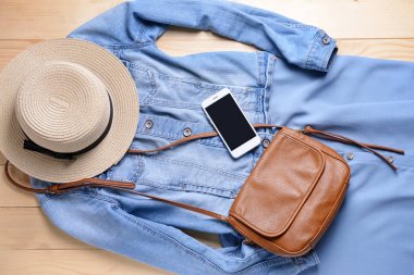 Ahşap arka planda şapka, çanta ve cep telefonu ile kadın giysiler