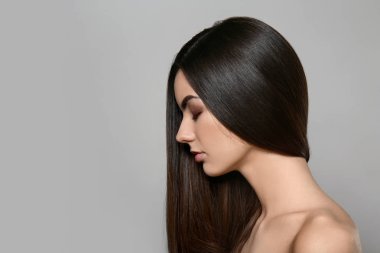 Gri arka planda sağlıklı uzun saçlı güzel genç kadının portresi