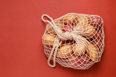 Renkli arka planda çiğ patatesli ip torbası.