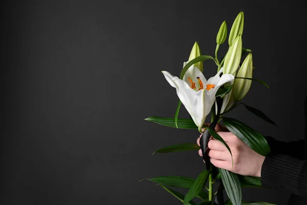 Mourning woman with lily flowers and black ribbon on dark background