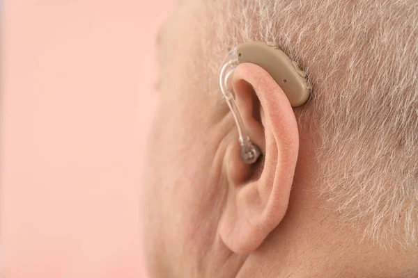 Senior man with hearing aid on color background, closeup — Stock Photo, Image