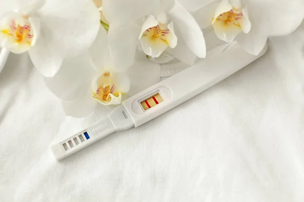 Positive pregnancy test and flowers on white cloth