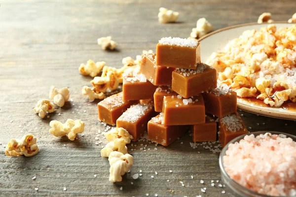 Tasty salty caramel candies with popcorn on wooden table — Stock Photo, Image